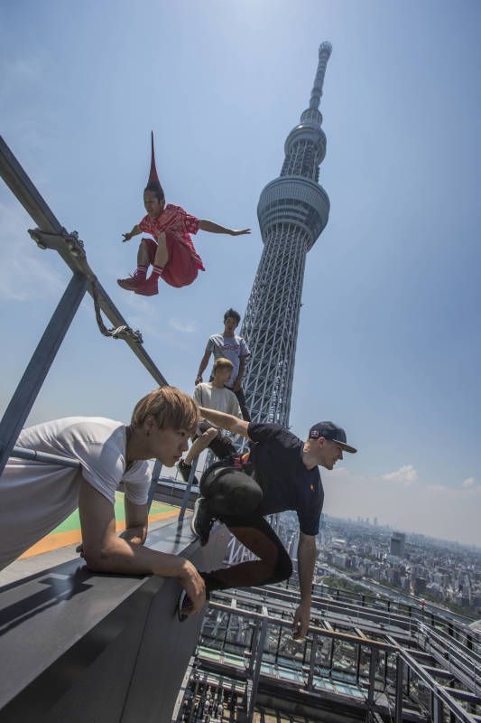 a group of young people are seen doing a parkour stunt on a rooftop. they are doing an incredible feat as they perch on a highrise building in the heart of tokyo.