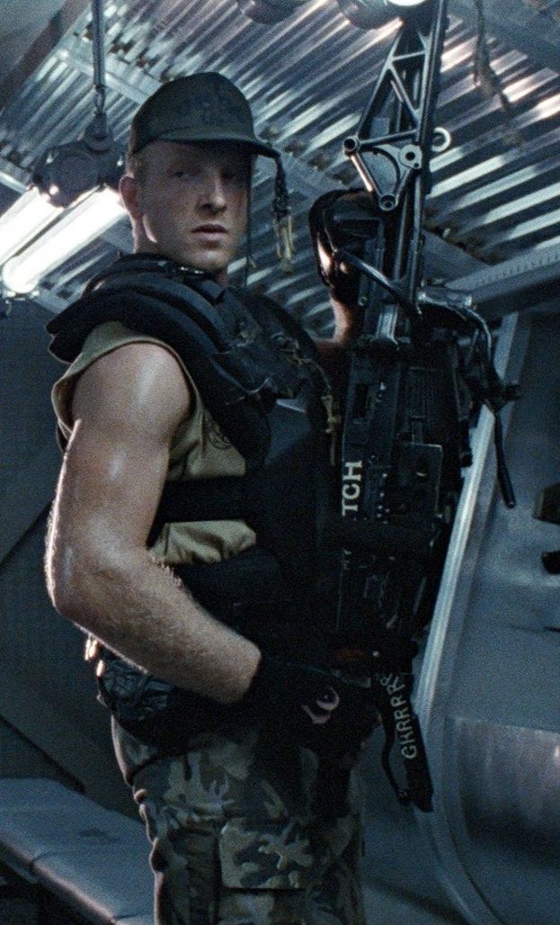 a soldier from the film aliens, wearing a helmet and military fatigues, stands holding a futuristic weapon. the soldier looks to be in combat mode with the weapon raised.  the film is set in space and the soldier is likely fighting aliens.
