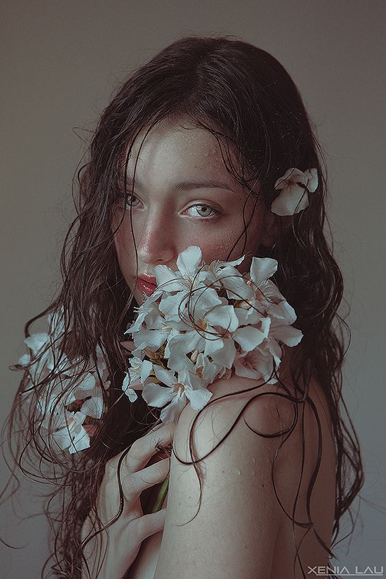 a woman with long, dark, wet hair partially obscures her face with a bouquet of white flowers. her gaze is directed towards the camera, creating a captivating and intimate portrait.  the lighting is soft and diffused, enhancing the overall ethereal atmosphere.