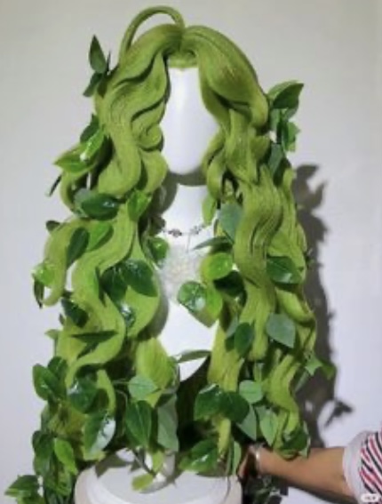 a vibrant green wig styled in voluminous waves and adorned with realisticlooking ivy and leaves. the wig is displayed on a white mannequin head, showcasing its intricate details and lush greenery.