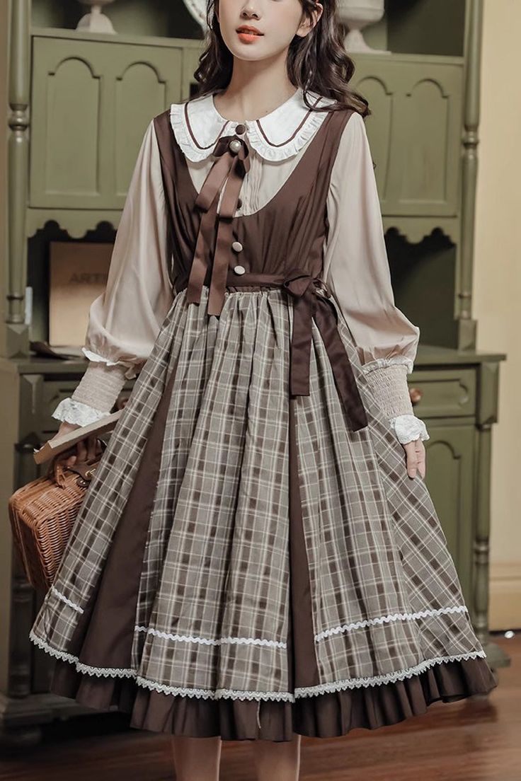 a woman is standing indoors wearing a brown and beige plaid lolita dress with a white blouse underneath. the dress has a peter pan collar and a ribbon tied at the neck. she is holding a wicker bag in her left hand. the lighting is soft and the perspective is eyelevel.