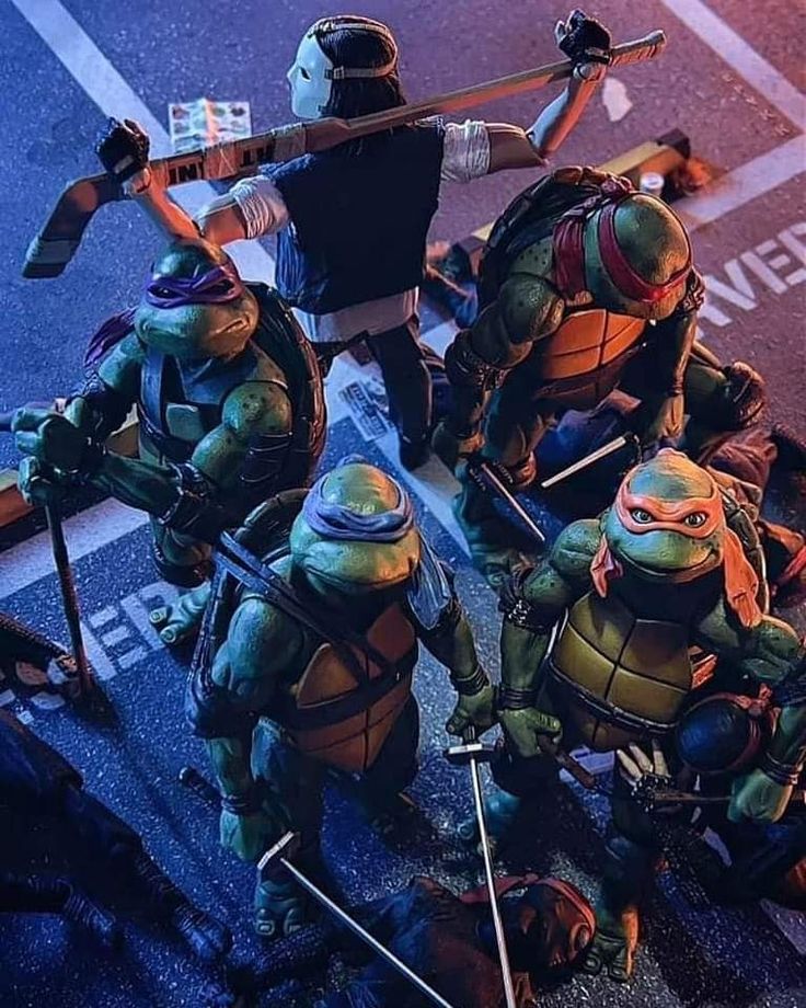 this image shows an actionpacked scene featuring the teenage mutant ninja turtles, four mutated humanoid turtles with ninja skills. there are 5 figures total in the image with  4 ninja turtles and one masked individual wielding a hockey stick.  the ninjas are dressed in their iconic green masks and outfits and wielding various weapons.