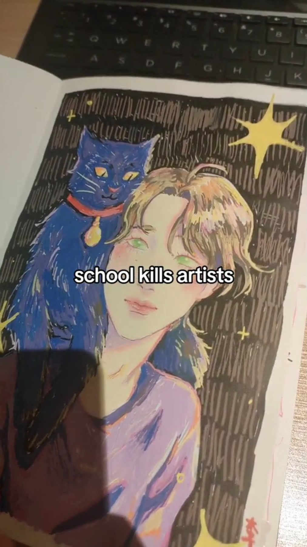 the image shows a vibrant, stylized drawing in a sketchbook of a person with short blonde hair and bright green eyes, holding a large blue cat with yellow eyes. the person is wearing a purple shirt. the drawing style is loose and expressive with visible brushstrokes.  the background is black with white scribbles and yellow starlike shapes. overlaying the drawing in a transparent white box is the text "school kills artists." the photo is taken indoors in artificial light, likely from overhead. a sliver of a laptop keyboard is visible at the top, suggesting the photo was taken by the artist in the midst of their process.