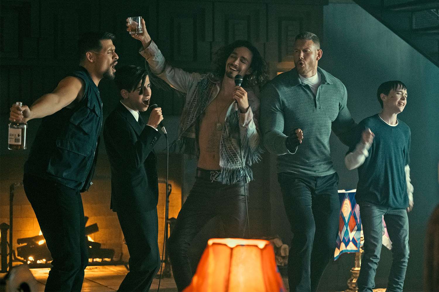 five people are exuberantly singing and dancing in a dimly lit living room. three adults and two children are captured midcelebration, with one adult holding a microphone and others holding bottles. a warm fire glows in the background, contributing to the overall festive and joyful atmosphere. the scene suggests a closeknit group enjoying a fun and carefree moment together.
