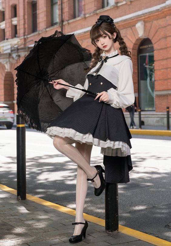a young woman wearing a black and white lolita fashion dress is standing on a city sidewalk, holding a black parasol. she is posing for the camera.