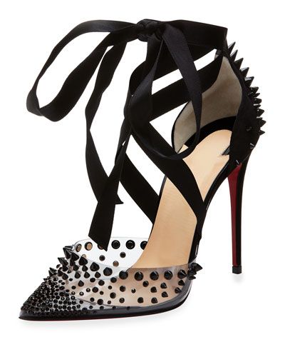 the image shows a pair of christian louboutin high heels.  they are black, stiletto heels with a transparent pvc upper adorned with black studs.  the shoes have a black ribbon that ties around the ankle in a crisscross pattern. the heel is the signature christian louboutin red. the overall style is glamorous and edgy.