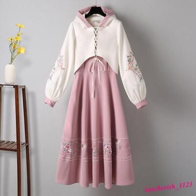 a pink dress with white floral embroidery. the dress has a laceup bodice and a flowing skirt. it is paired with a white hoodie with long sleeves and floral embroidery on the sleeves. the hoodie is cropped and has a laceup front.