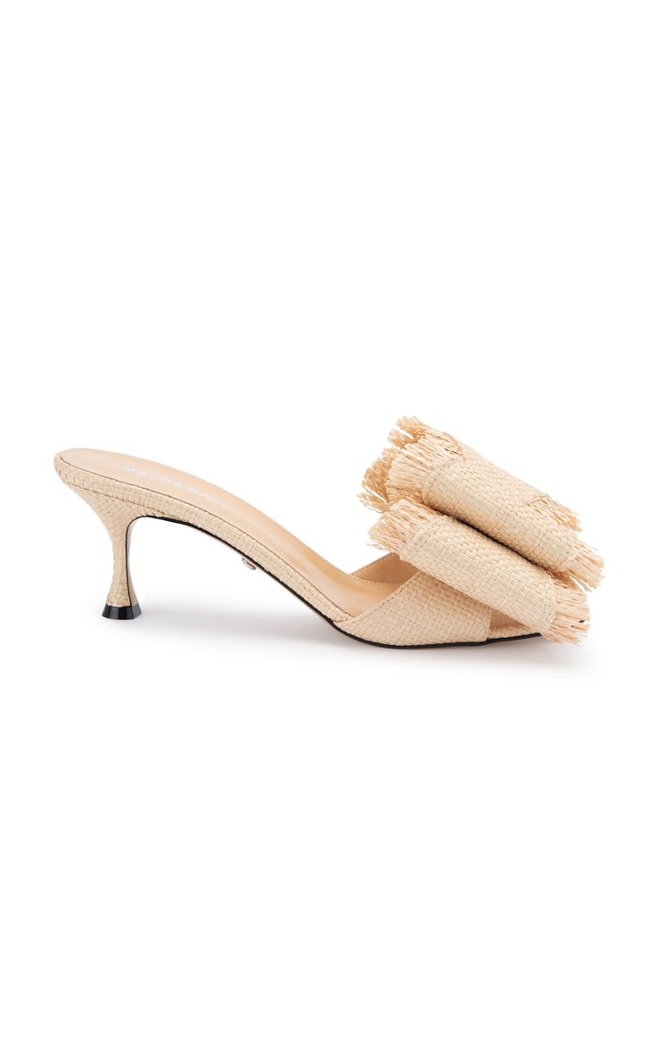a pair of beige raffia heeled mules with a bow detail on the top. the shoes are shown on a white background. the bow is made of the same material as the shoes and has a frayed edge. the heels are thin and stilettolike. the shoes are elegant and stylish, perfect for summer.
