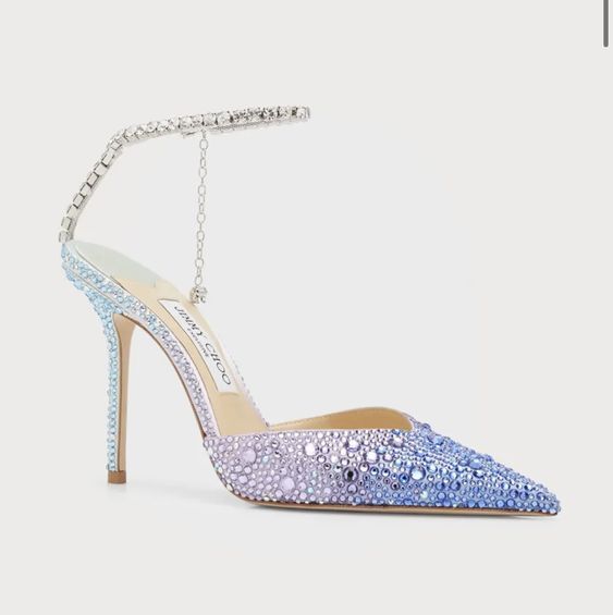 the image shows a single jimmy choo women's high heel shoe. the shoe is a pointedtoe slingback style with an ankle strap adorned with crystals. the crystals create an ombre effect, transitioning from a light purple to a light blue across the shoe. the heel is stiletto, and the overall design is elegant and sparkly. the shoe is presented against a plain white background, highlighting its details.