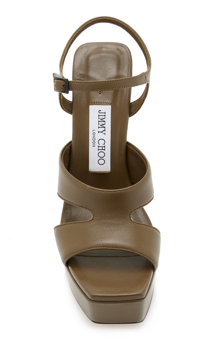 a pair of olive green leather jimmy choo platform sandals with an ankle strap and cutout detail is shown in the image. the sandals have a square toe and are positioned so that the top and the front of the shoes are visible.  the jimmy choo london label is visible on the insole.