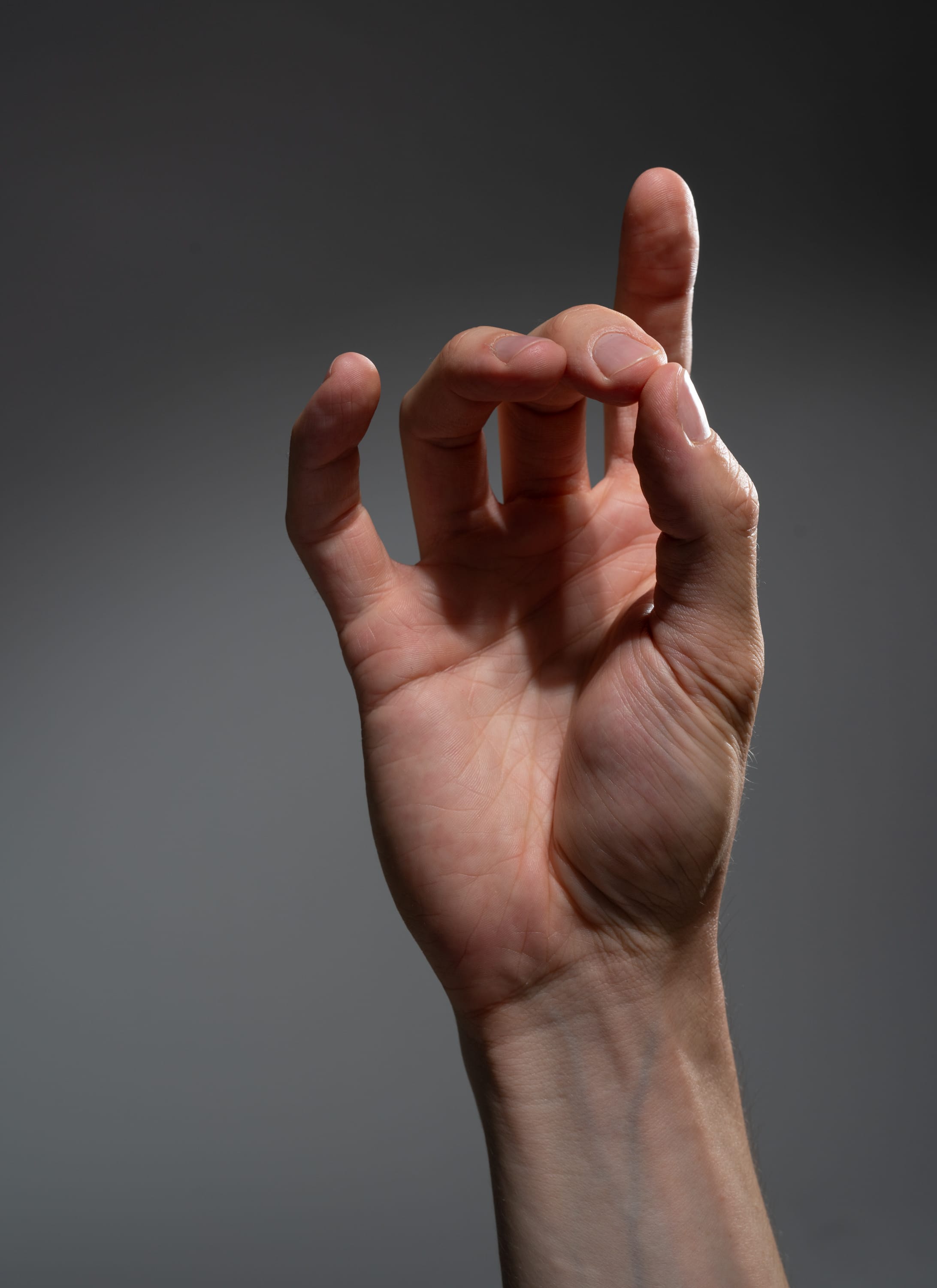 a male hand is making a pinching gesture against a gray background. the lighting is soft and highlights the details of the hand.