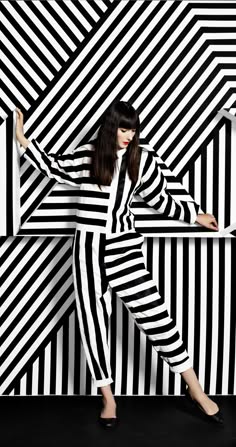 a woman wearing a black and white striped jumpsuit poses in front of a black and white striped wall.