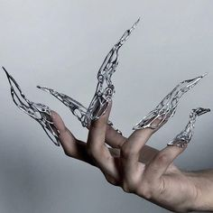 a closeup image showcases an individual's hand adorned with intricately designed silver clawlike nail enhancements. the nails are long, sharp, and resemble the claws of a fantastical creature. the lighting is soft and highlights the metallic sheen of the nail art.  the image focuses on the hand and nails, blurring the background and emphasizing the intricate details of the nail design.