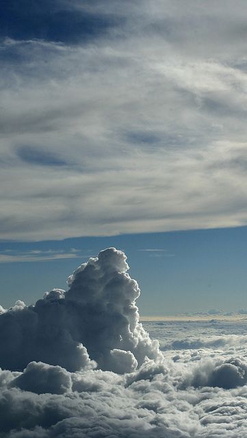 this image shows a beautiful view of clouds from an airplane window.  a large cumulus cloud dominates the center of the frame.  the cloud is bathed in sunlight and casts shadows on the surrounding clouds, creating a dramatic and textured scene.  the bright blue sky above peeks through the fluffy white clouds.  this image captures the wonder and beauty of nature from a unique perspective.