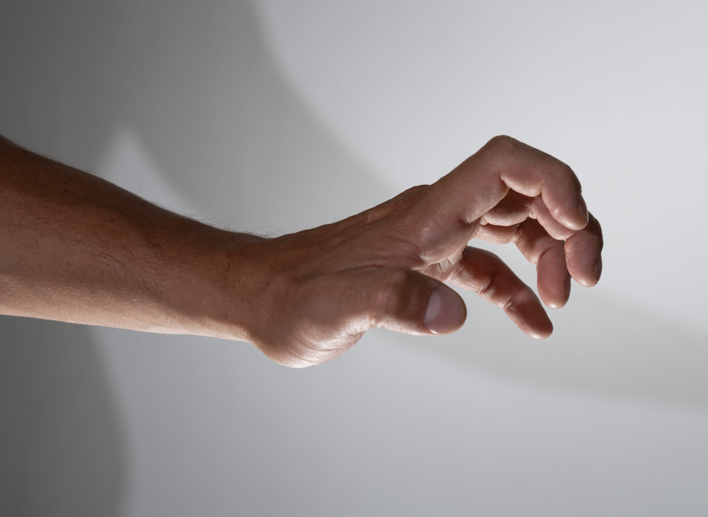 a closeup view of a man's outstretched hand and arm set against a plain background. the hand is partially open, fingers curled as if reaching or grasping for something. the studio lighting casts distinct shadows, emphasizing the contours and gesture of the hand.