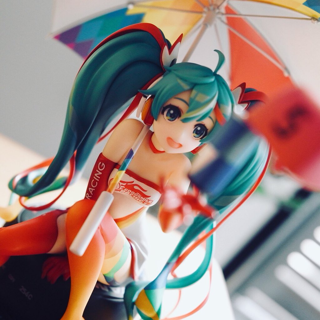 low angle shot of a hatsune miku figurine in her racing outfit holding a colorful umbrella.