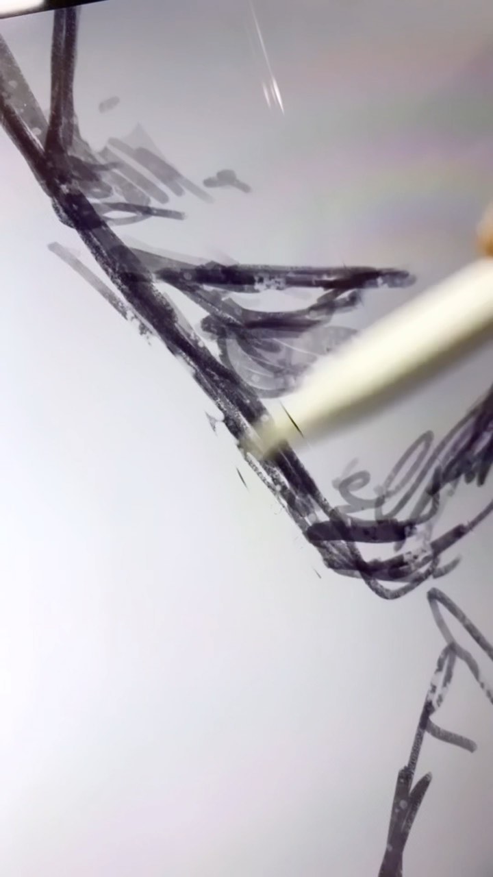 closeup view of a hand holding a stylus and drawing on a digital tablet. the drawing is abstract and consists of dark, expressive lines and shapes on a light background. the focus is on the hand and stylus as they create the artwork. the image shows the process of digital art creation.