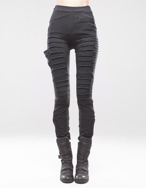 a person is shown from the waist down, wearing black futuristiclooking pants with folds and pockets. the pants are highwaisted and fitted. the person is also wearing black boots with straps and buckles. the background is white.