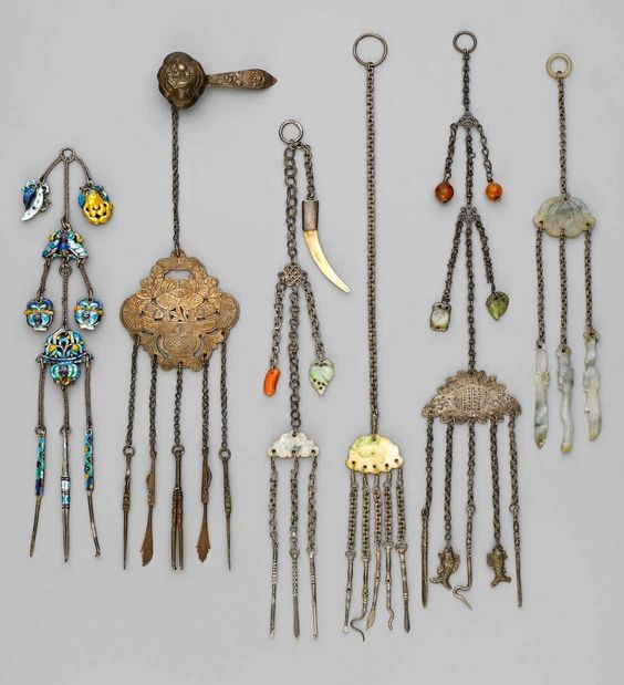 the image shows a collection of antique asian jewelry, primarily ornaments and earrings. they are made with materials such as silver, gold, precious stones, beads, and enamel. the pieces are ornate and feature intricate designs with chains, pendants, and tassels. they appear to be historical artifacts.
