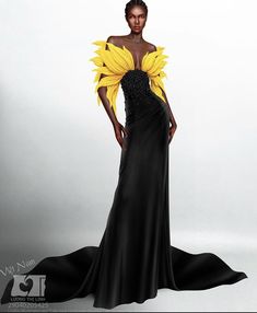 a woman in a black gown adorned with sunflower petals is standing with her right hand on her hip and her left hand on her side, posed in a studio with a plain white backdrop.