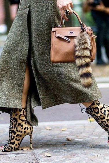 a stylish woman in a green tweed coat and leopard print ankle boots is walking down the street. she is carrying a brown hermes kelly bag with a fluffy fur keychain.  the image showcases highfashion street style and focuses on the details of the outfit and accessories. the overall aesthetic is elegant and sophisticated.