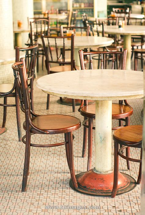 a vintagestyle cafe interior with a wooden chair and round marble table. the floor is tiled and there are other chairs and tables in the background, making the space cozy and inviting. the chair is sturdy with a wooden frame and darkbrown finish. the table is a classic, with a smooth, white surface and a single, central leg that supports the top.  the image captures a sense of nostalgia and timeless elegance, perfect for a relaxing coffee break or a leisurely lunch.