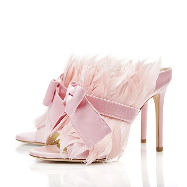 two pink highheeled shoes are adorned with feathers and bows. the shoes have a satin finish and are positioned on a reflective surface against a white background. they appear to be a fashionable and luxurious item.