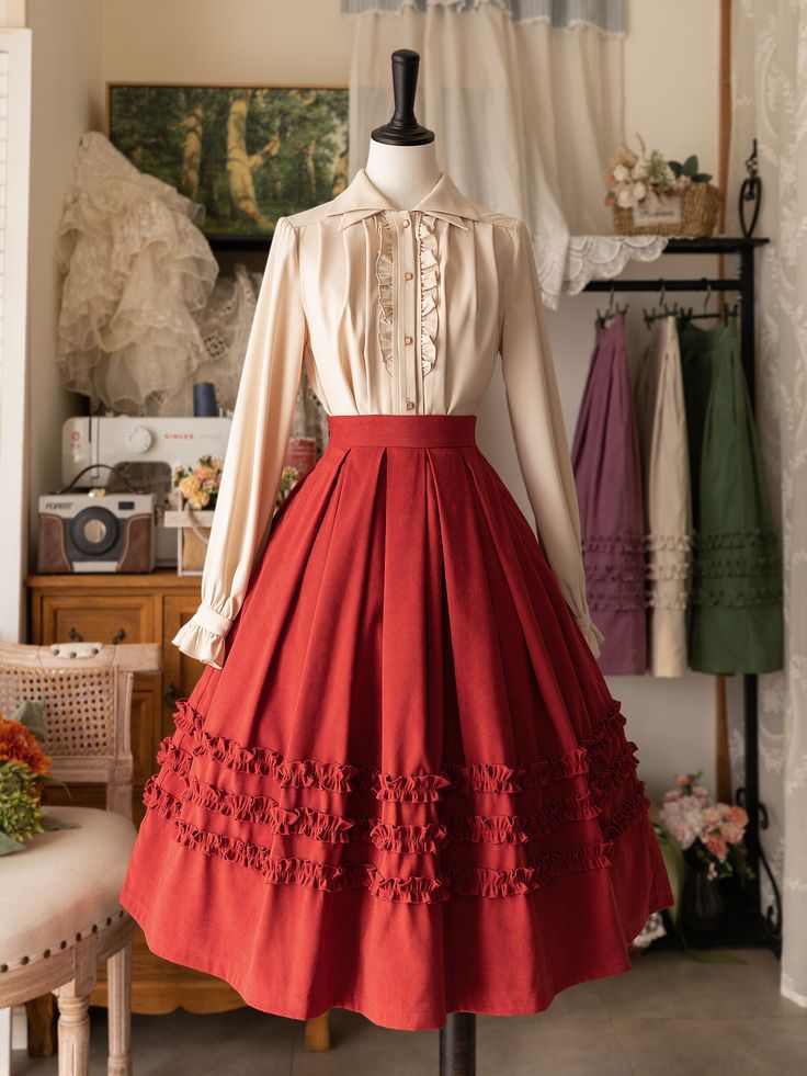 a mannequin stands in a sewing room, dressed in a vintageinspired lolita fashion outfit. the outfit features a flowing ivory blouse with delicate buttons and a full, highwaisted red skirt with cascading ruffles. the warm lighting highlights the rich colors and textures of the clothing, creating a romantic and whimsical atmosphere.