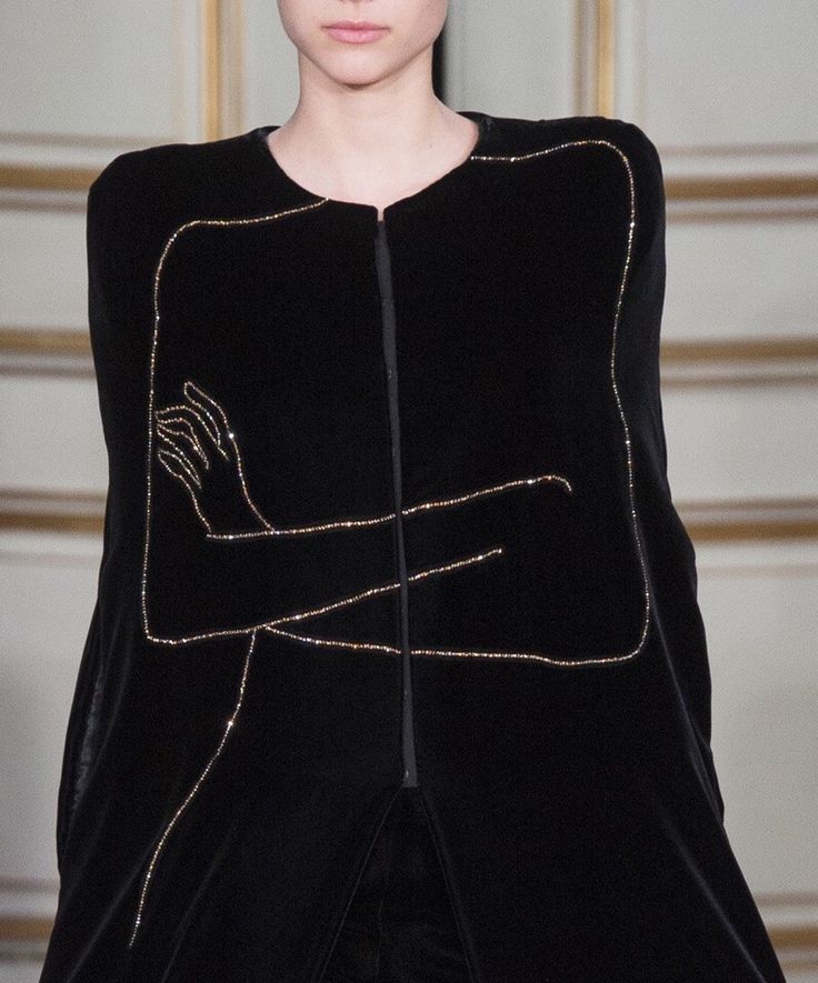 a closeup view of a woman wearing a black velvet dress with gold embroidered detailing. the dress features a unique design with the outline of a person's arms and hands embroidered in gold rhinestones. the dress is a sophisticated and elegant piece, ideal for a special occasion. the image captures the intricate details and craftsmanship of the garment.