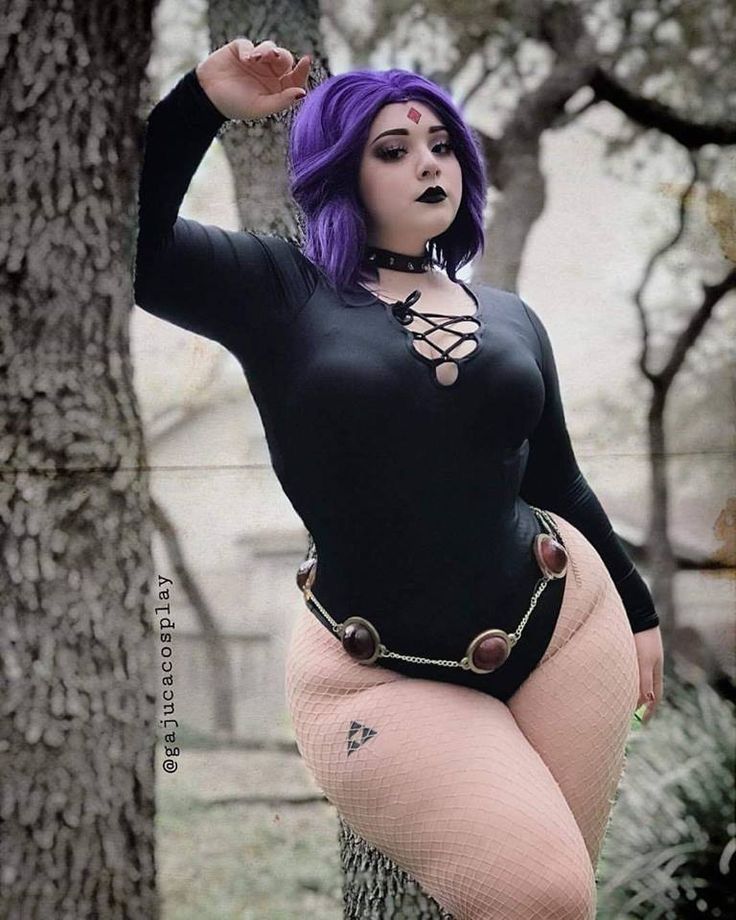 a woman dressed in a raven cosplay outfit is leaning against a tree. she has purple hair, black lipstick, and wears a black choker and leotard. a jeweled belt accentuates her waist. she's wearing fishnet stockings and has a tattoo on her thigh. the backdrop features trees in an outdoor setting.