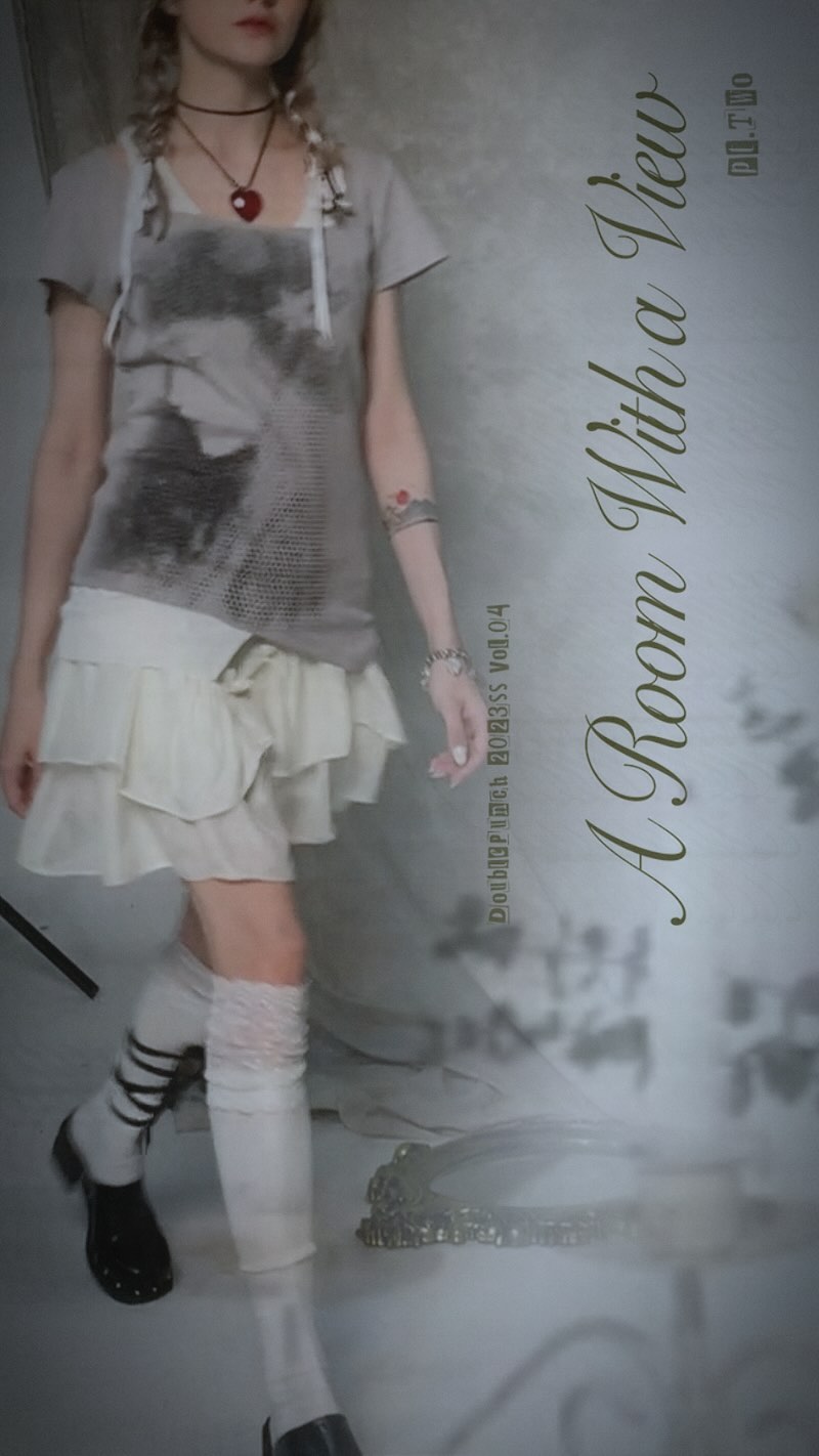 a fulllength shot of a pale young woman with blonde pigtails wearing a grey and white ruffled dress, white socks, and black shoes. she is posing against a light grey backdrop, and the image has a dreamy, vintage aesthetic.  the text "a room with a view" is prominently displayed, along with additional smaller text. the overall style is reminiscent of lolita fashion,  and the image appears to be a professional photoshoot.