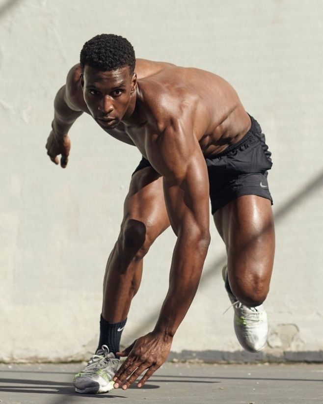 a shirtless, athletic man in black shorts is in a running pose,  with his muscles flexed and ready for action.  his focused expression shows his determination, while his muscular physique highlights his strength and fitness. he's poised to  take off and conquer his goal.