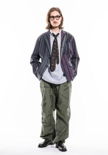 a fullbody studio shot of a man modeling a casual outfit. he is wearing a striped vintagestyle jacket, a patterned shirt, a tie, patterned pants, and black shoes. the man is standing with his hands in his pockets, and he is looking slightly to the side.  the background is plain white.  his style is a blend of vintage and casual.