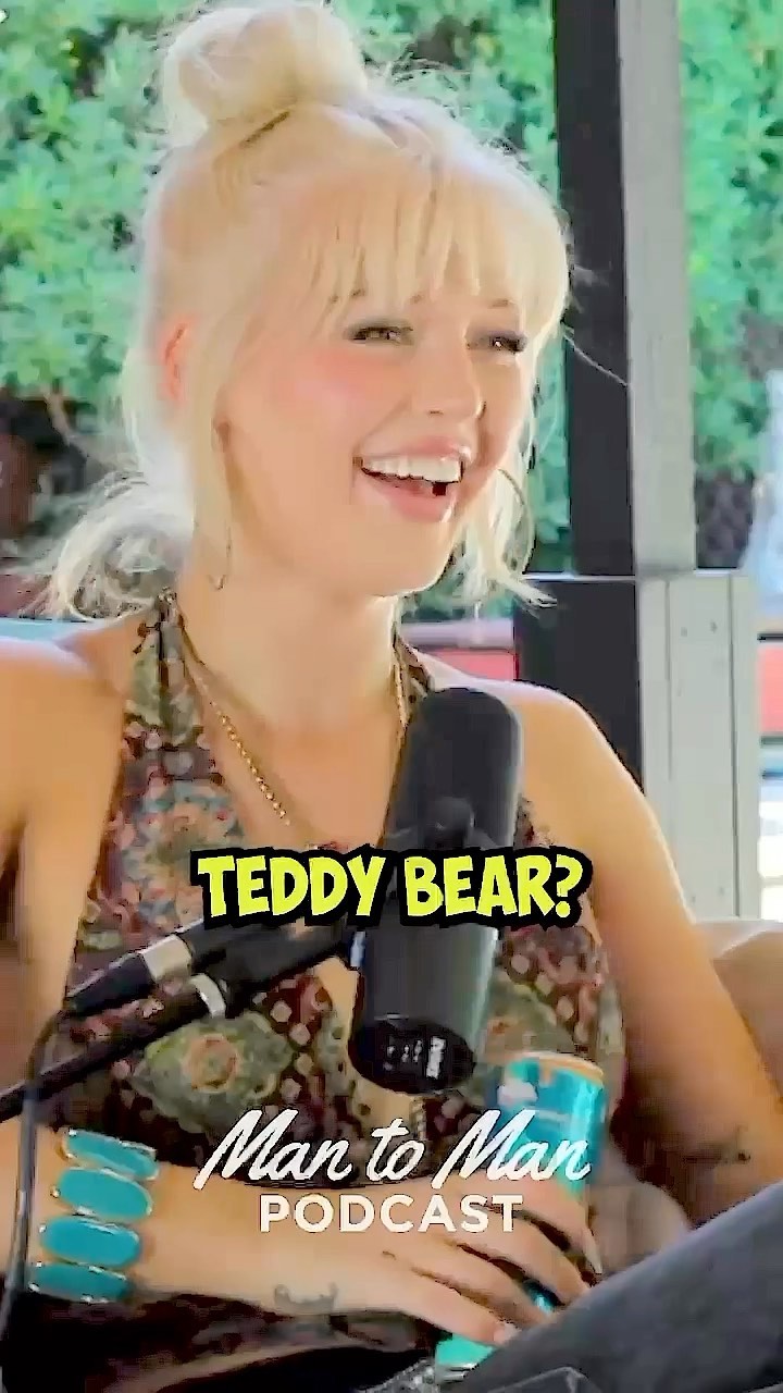 a fairskinned woman with blonde hair in an updo is speaking into a microphone. she is wearing a halter top and a bracelet of large blue stones. she also has a tattoo on her wrist. a can sits on the table in front of her. the words "teddy bear?" and "man to man podcast" are superimposed on the image.