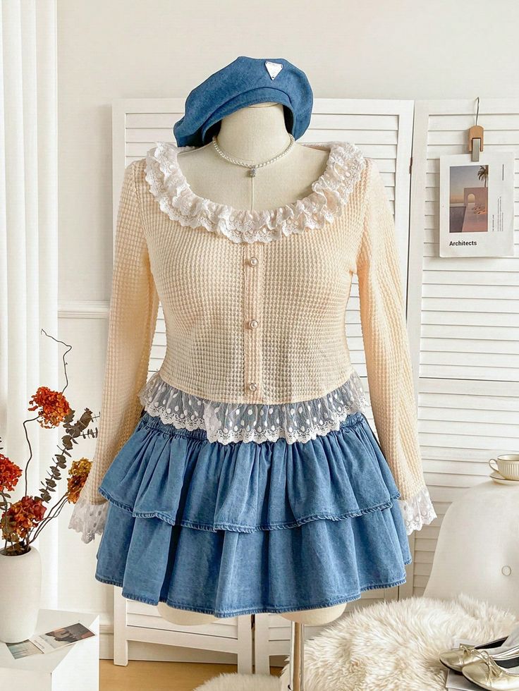 a creamcolored knit top with lace trim and pearl buttons, paired with a blue denim ruffle skirt, is displayed on a mannequin. the mannequin is wearing a blue beret and a delicate necklace.  the outfit is set against a plain backdrop with a small shelf displaying a picture and dried flowers. the scene is welllit, likely with studio lighting, to highlight the details and textures of the outfit.