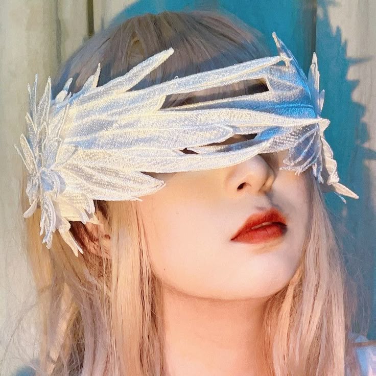a portrait of a woman wearing a white, feathery blindfoldstyle mask that covers her eyes. she has fair skin, blond hair, and is wearing red lipstick.
