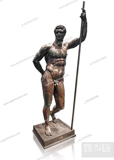 the image shows a bronze statue of a nude man, standing on a square pedestal. the man is holding a staff in his right hand, his left hand is on his hip. he has short curly hair and a muscular physique. the statue is lit from the front and slightly from above, which creates a sense of depth and dimension. the background is plain white.