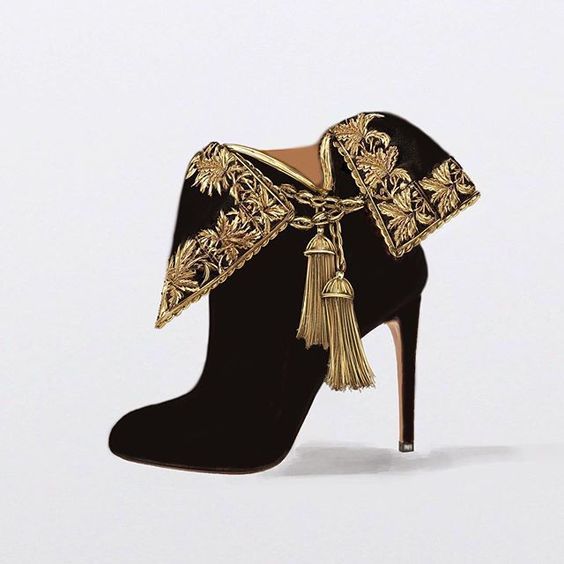the image showcases a pair of elegant women's ankle boots.  the boots are made of black velvet and feature a striking gold embroidered detail that forms a collarlike element around the top of the boot.  the embroidery is intricately designed with floral or leaflike patterns.  hanging from the center of the collar are gold tassels, adding to the luxurious and ornate appearance. the boots have a high stiletto heel and are presented against a plain white background, highlighting the intricate details of the design. the overall style is luxurious and fashionforward.