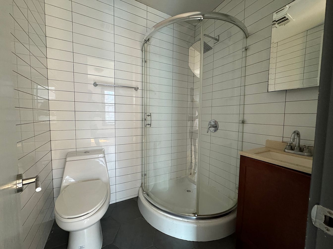 a small bathroom with white subway tile walls, a white toilet, a glassenclosed shower, a white sink, and a brown cabinet. the shower has a chrome shower head and a chrome handle. the sink has a chrome faucet and a white countertop. the vanity is brown with a white countertop.
