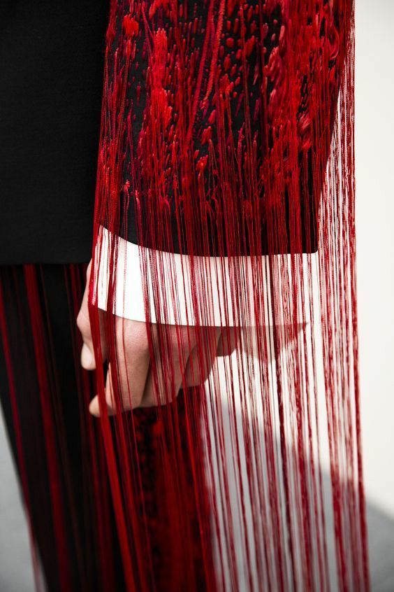 a closeup shot of a red fringed garment. the fabric has a dark red base with a thin, even fringe. the fringe is long and flowing, creating a dramatic effect.