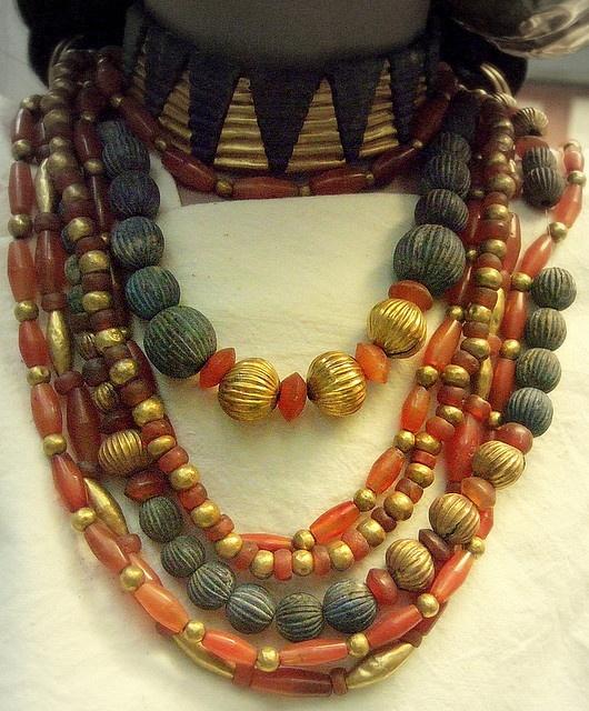 a closeup of multiple strands of ancient egyptian jewelry, featuring a pectoral collar necklace and layered beaded necklaces made of carnelian, lapis lazuli, and gold.