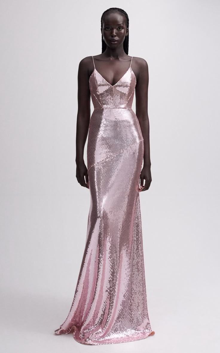 a darkskinned woman is standing in front of a white background wearing a light pink floorlength sequin gown with spaghetti straps.