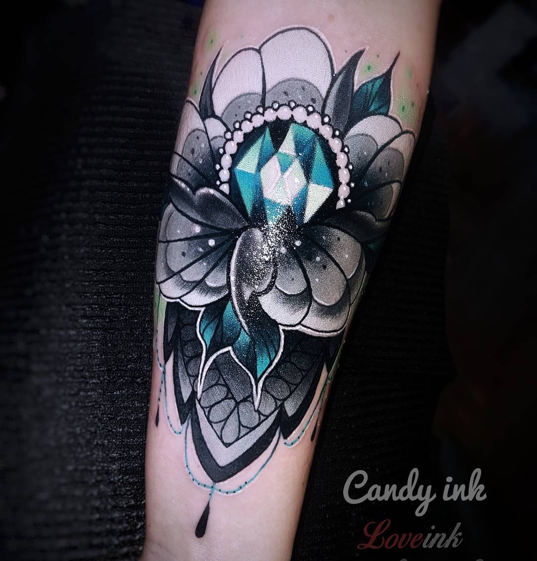 a temporary tattoo of a jewel centered in a flower mandala on a person's forearm.  the tattoo is rendered in black, white, teal, and mint green, and accented with glitter.  the image is watermarked with the text "candy ink love ink" in white and pink.