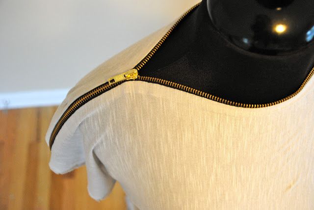 a closeup shot of a lightcolored tshirt with a gold zipper around the neckline, displayed on a mannequin.