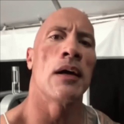closeup of dwayne "the rock" johnson with a confused expression and raised eyebrow. he is bald and appears to be in a gym setting, as gym equipment is visible in the background.