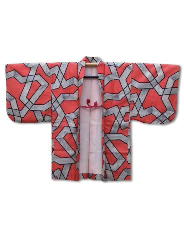 an open japanese kimono in coral, red, gray, silver, and black is hanging against a white background. the kimono has a geometric pattern throughout. the sleeves are wide and long. the kimono is open and reveals a light pink lining. a wooden hanger is visible at the top of the kimono. two red tassels are tied at the front.