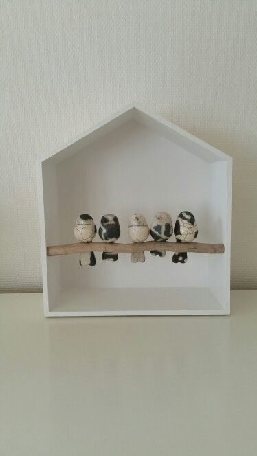 a white houseshaped shelf with five decorative ceramic bird sculptures perched on a branch inside. the shelf is sitting on a white surface.