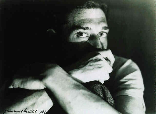 the image is a black and white closeup portrait of a man.  he appears to be seated and is shown from the chest up. his arms are crossed tightly across his chest, and his hands are covering a significant portion of his face, obscuring his mouth and nose.  only his eyes and forehead are clearly visible, conveying a sense of worry, pensiveness, or sadness. the lighting is dramatic, with strong shadows adding to the emotional intensity of the portrait. the photograph is signed "emmanuel hill 1983" in the bottom left corner.  the overall mood is dark and introspective.