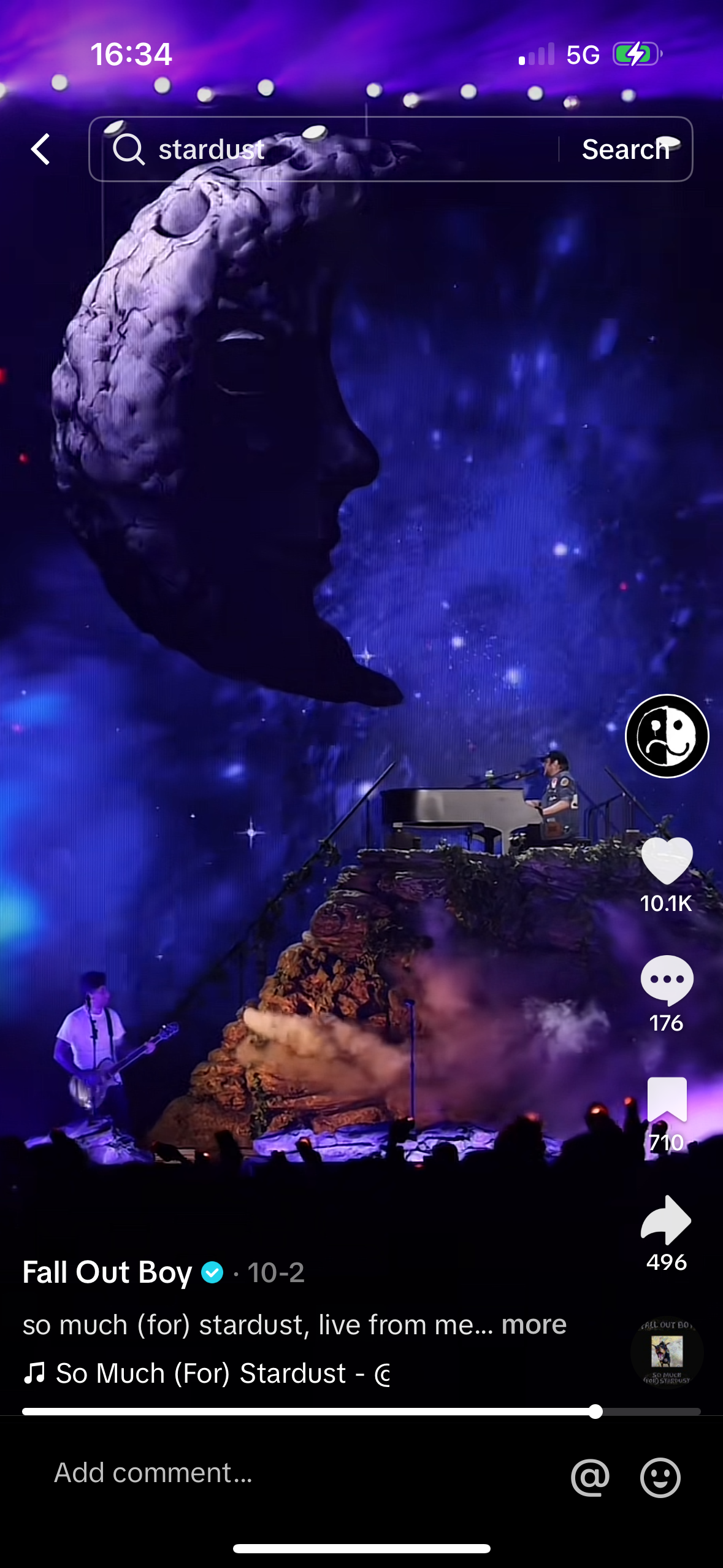 this is a screenshot of a mobile phone showing a fall out boy music video. the video is titled "so much (for) stardust" and shows the band performing live on a stage.  the image is from a social media app where you can like, comment, and share. the band's song is playing in the background and the video is paused.