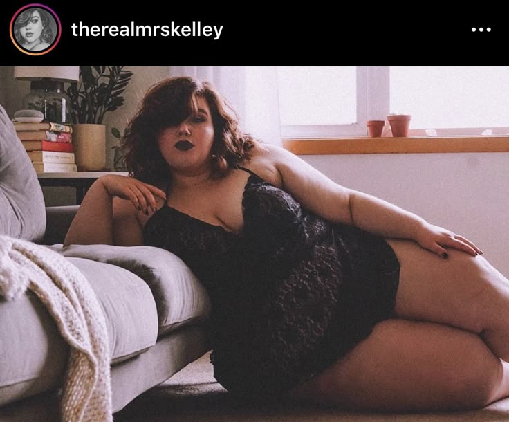 a woman in black lingerie is lying on a couch and the floor. there is a blanket on the couch next to her. behind the couch is a side table with plants and books. there is a window behind the side table. the top of the image shows an instagram post from user "therealmrskelley."